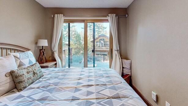Un dormitorio con cama, mesita de noche, lámpara, ventana con cortinas y vista a un edificio.