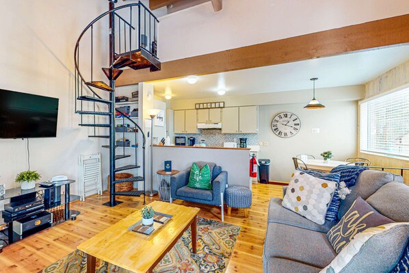 A modern living room with a spiral staircase, a sofa, a coffee table, and a kitchen area in the background. - Family-Friendly Condo with Pool, Tennis, Deck & Walk to Beach Access (Kings Beach)