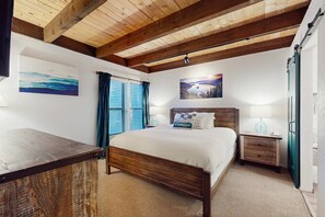 A bedroom with a wooden bed, a nightstand, a desk, and a window with curtains. - Welcome to a quintessential mountain hideaway, brimming with Lake Tahoe charm (South Lake Tahoe)