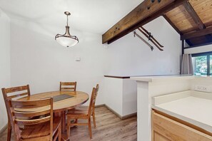 A dining area with a wooden table and chairs, a hanging light fixture, and a kitchen counter with a window. - Welcome to a quintessential mountain hideaway, brimming with Lake Tahoe charm (South Lake Tahoe)