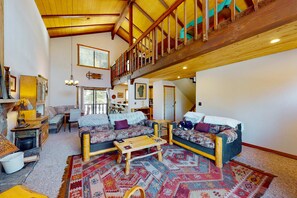 Ein geräumiges Wohnzimmer mit hoher Decke, Holzbalken, einer Treppe und einem großen Fenster.