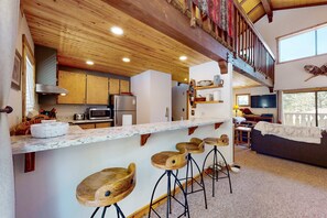 Eine moderne Küche mit Holzbarhocker, ein Essbereich mit einer Couch und ein Balkon mit Geländer.
