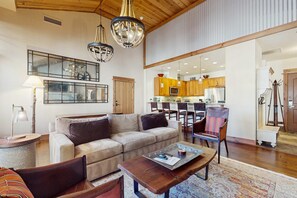 Ein geräumiges Wohnzimmer mit einer großen Couch, einem Couchtisch und einem Essbereich mit Holzkreisen sowie einer Küche im Hintergrund.