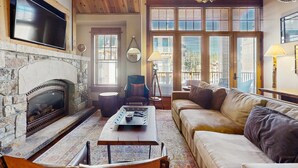 Una sala de estar con chimenea de piedra, un sofá, una mesa de centro y ventanas grandes con persianas.