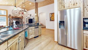 A modern kitchen with wooden cabinets, a stainless steel refrigerator, and a stone fireplace. - Wooded Luxury at Modern Tahoe Donner Retreat with Private Deck in the Pines (Truckee)