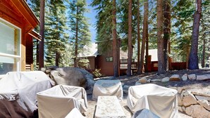 A covered outdoor seating area with tables and chairs, surrounded by trees and a cabin. - Wooded Luxury at Modern Tahoe Donner Retreat with Private Deck in the Pines (Truckee)