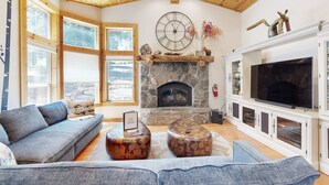 A spacious living room with a stone fireplace, a large TV, and a modern sofa. - Wooded Luxury at Modern Tahoe Donner Retreat with Private Deck in the Pines (Truckee)