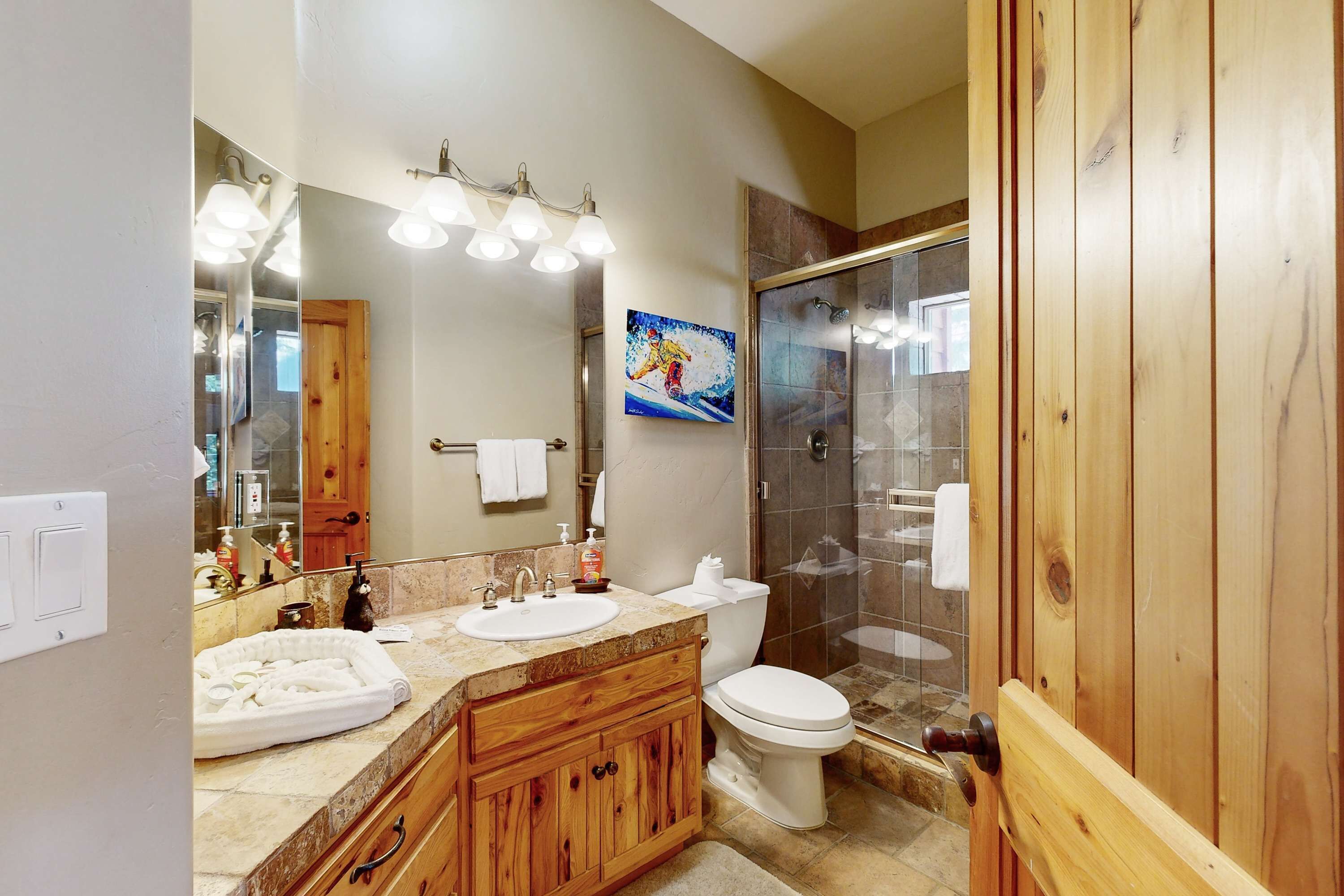 A bathroom with a wooden vanity, a sink, a toilet, a shower with glass doors, and a large mirror.