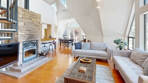 A spacious living area with a fireplace, a sofa, a coffee table, and a dining area in the background.