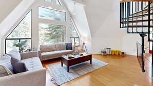 A spacious loft with high ceilings, large windows, a wooden staircase, and a cozy seating area.