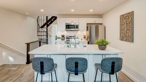 Uma cozinha moderna com uma ilha central, banquetas, uma escada e um elemento decorativo na parede.