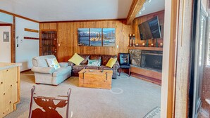 A living room with a wooden wall, a sofa, a coffee table, a television, and a fireplace. - Rustic mountain view condo w/ full kitchen - walk to lifts (Olympic Valley)