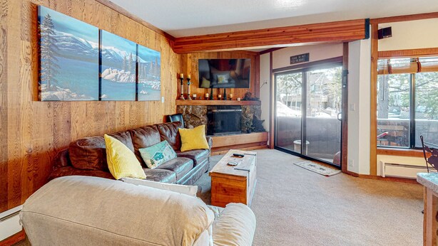 A cozy living room with a fireplace, wooden walls, a large TV, and a sliding glass door to the outside. - Rustic mountain view condo w/ full kitchen - walk to lifts (Olympic Valley)