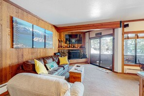 Una sala de estar acogedora con chimenea, paredes de madera, un televisor grande y un ventanal corredero al exterior.