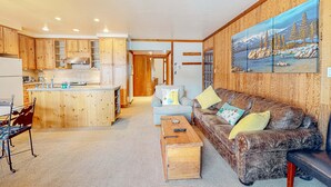 A modern kitchen with wooden cabinets, a central island, and a dining area with a metal chair and table. - Rustic mountain view condo w/ full kitchen - walk to lifts (Olympic Valley)
