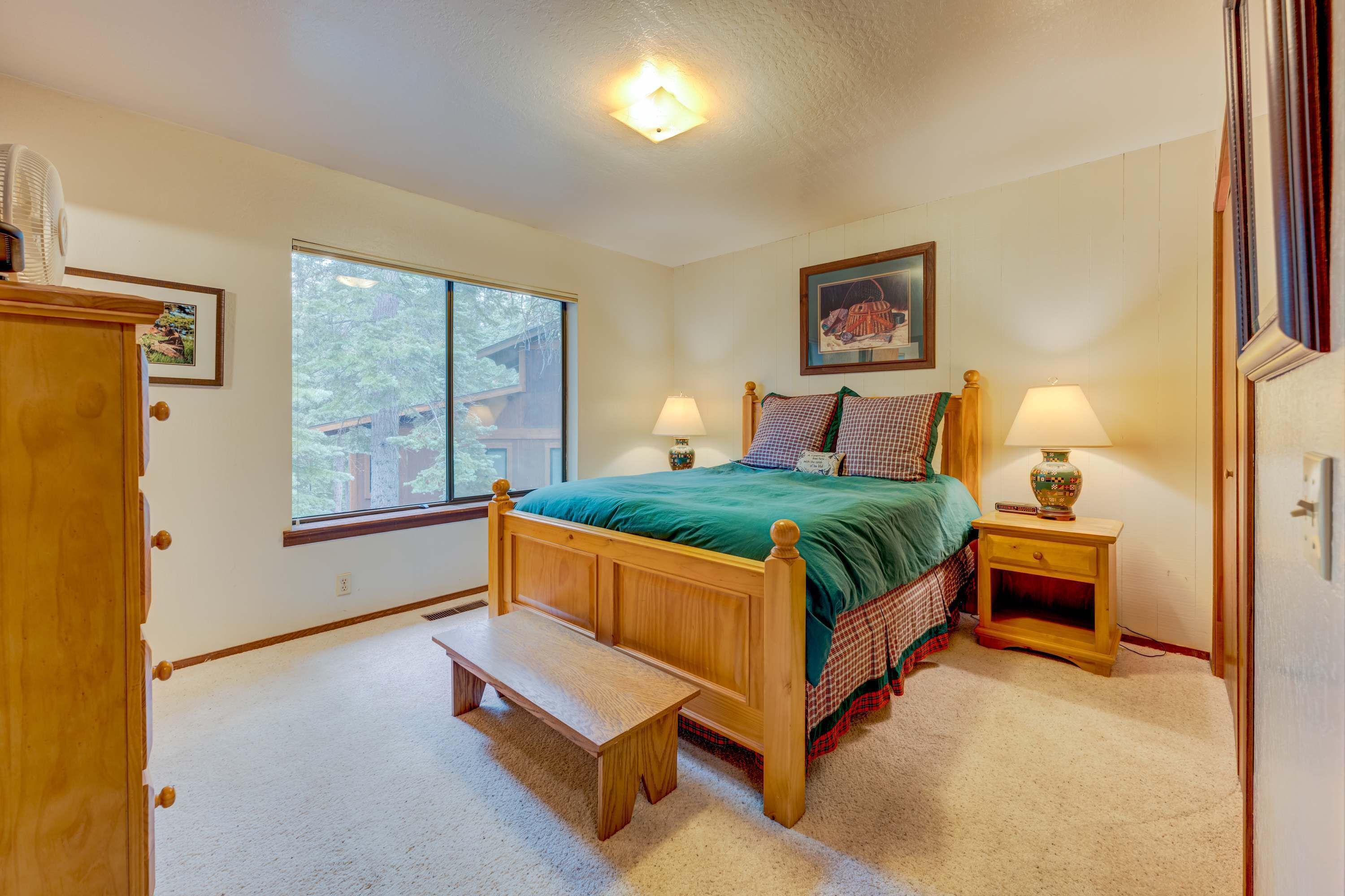A bedroom with a wooden bed, a bench, a nightstand, a window, and a door.