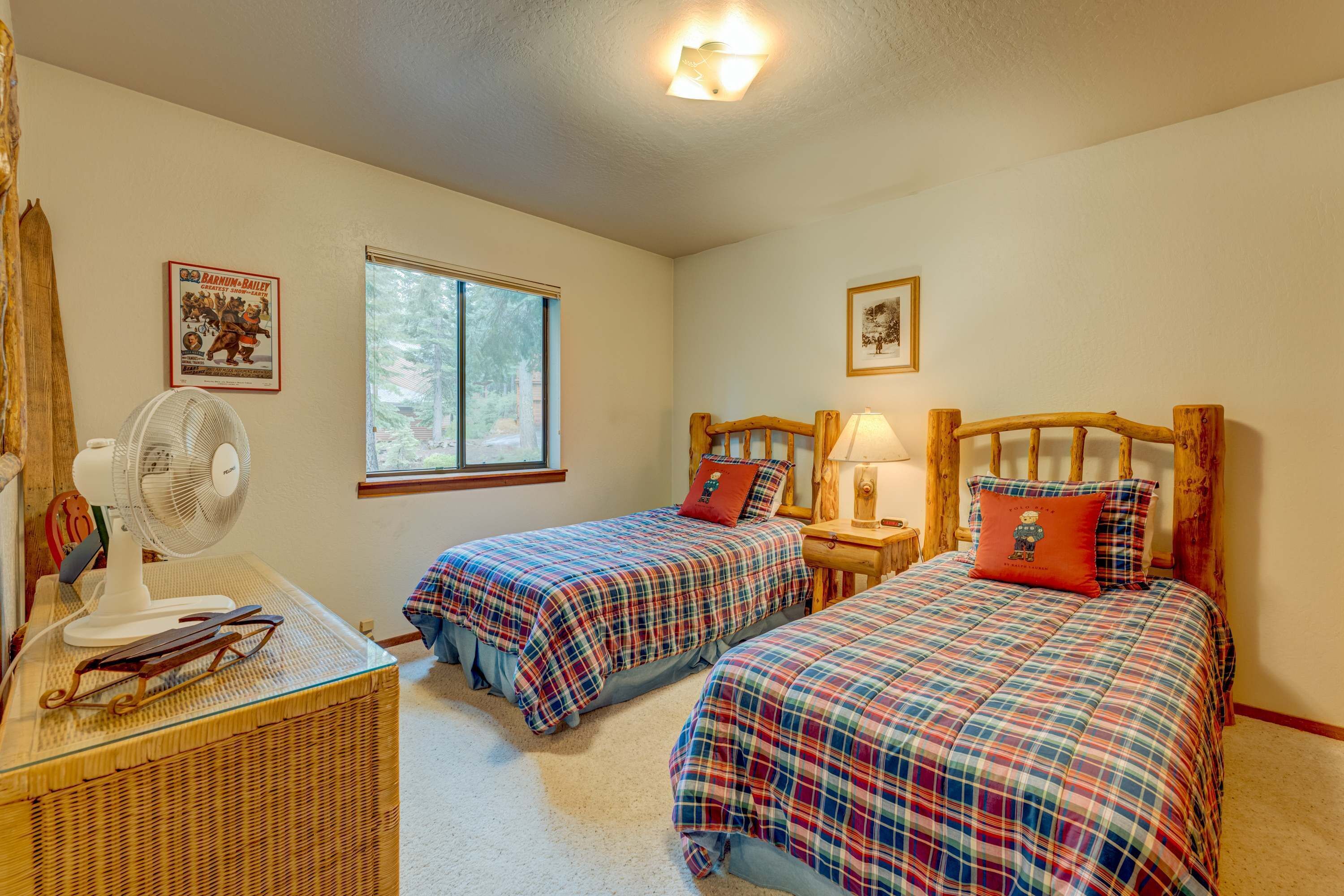 A bedroom with two beds, a fan, a wicker basket, and a window.