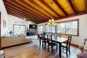A spacious living area with a wooden ceiling, a fireplace, a dining table with chairs, and large windows. - Lovely tree-view condo with deck, grill, & fireplace - near Tahoe City & lake (Tahoe City)