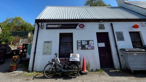 A small white building with a metal roof, a sign for a post office, and a bicycle parked in front. - Room-charming Guest Room in the Beautifu (Isle of Mull)