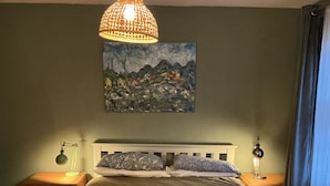 A bedroom with a bed, two bedside tables, a hanging lamp, a painting, and a window with curtains. - Room-charming Guest Room in the Beautifu (Isle of Mull)