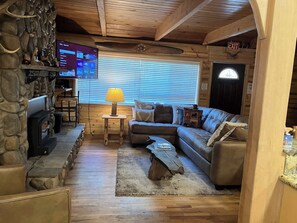A cozy cabin interior with a stone wall, a fireplace, a television, a sofa, and a lamp. - Inviting home with pool table - near Heavenly & beaches (South Lake Tahoe)