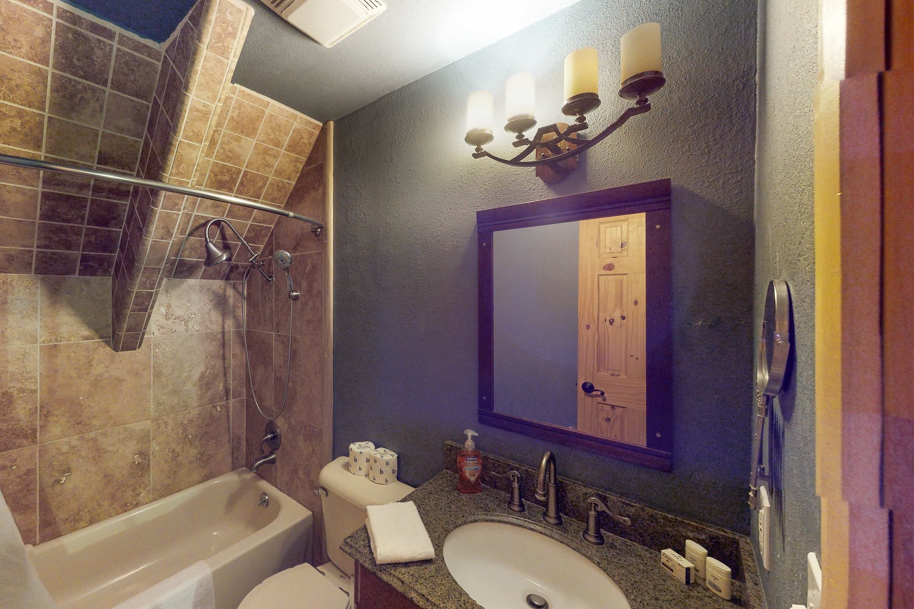 Une salle de bain équipée d’une baignoire, de toilettes, d’un lavabo et d’un miroir qui reflète la porte.
