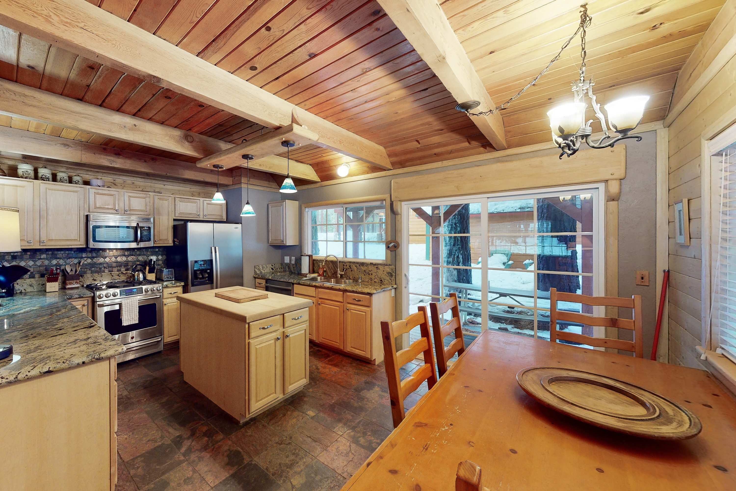 A kitchen with wooden beams, granite countertops, stainless steel appliances, and a dining area with a wooden table and chairs.