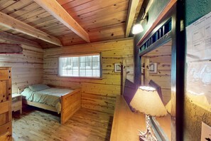 A wooden cabin room with a bed, a window, a lamp, and a mirror. - Walkup Pines (South Lake Tahoe)