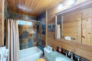 A bathroom with a bathtub, toilet, and sink, wooden walls, and a mirror. - Walkup Pines (South Lake Tahoe)