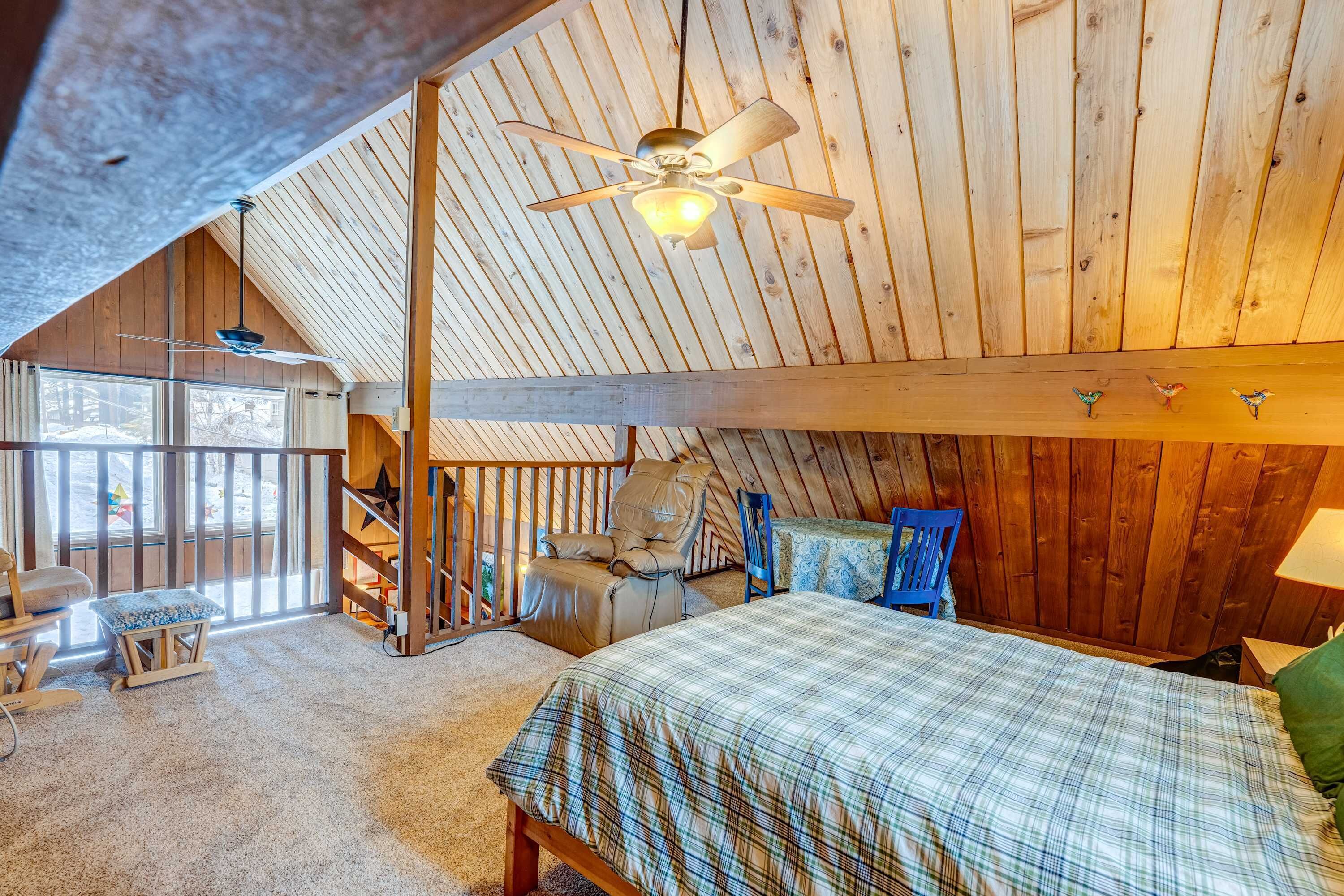 A cozy attic bedroom with a bed, a chair, a desk, and a ceiling fan.