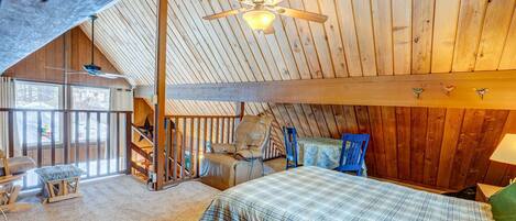 A cozy attic bedroom with a bed, a chair, a desk, and a ceiling fan.