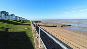 A coastal area with a grassy slope, a metal railing, and a beach. - Ocean Breeze Escape (Rochester)