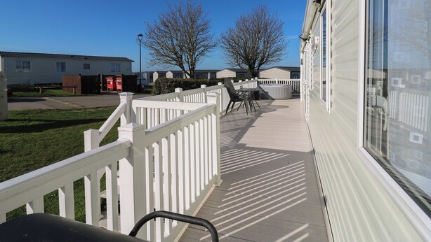 A covered outdoor area with a white fence, a hot tub, and a patio table. - Ocean Breeze Escape (Rochester)