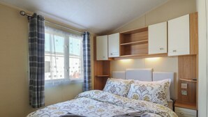 A bedroom with a bed, curtains, a window, and built-in cabinets. - Ocean Breeze Escape (Rochester)