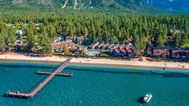 Eine Luftaufnahme eines Küstenresorts mit einer Mole, klarem türkisblauem Wasser und einer Kulisse aus dicht bewaldeten Bergen.