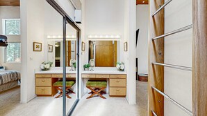A room with a mirrored vanity, wooden drawers, a bench, and a large mirror with lights. - Modern mountain home with private hot tub, deck, fireplace, & skiing nearby (Northstar - Truckee)