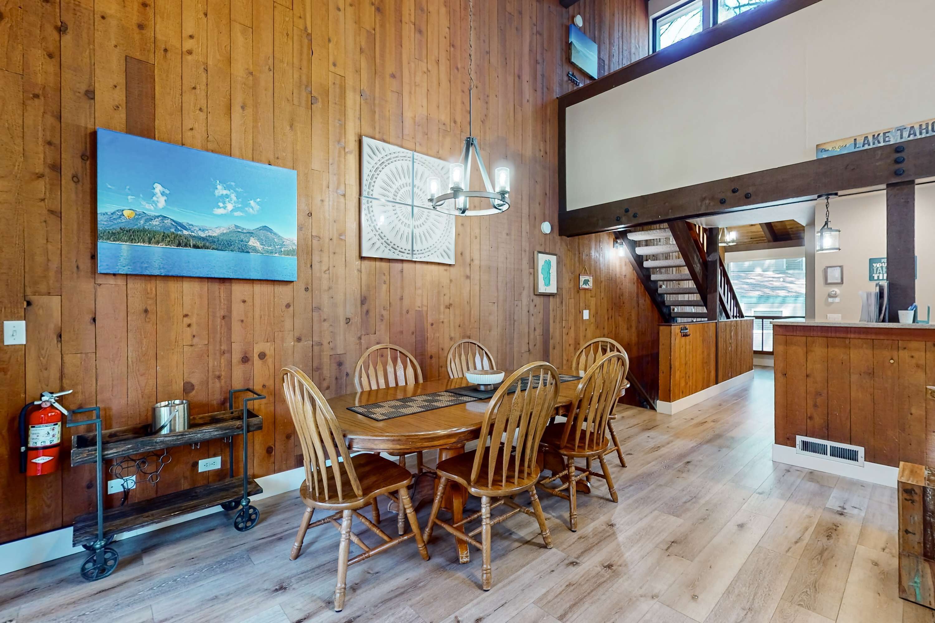 A wooden dining area with a table and chairs, a chandelier, a painting, and a sign reading 'LAKE TAHOE'.