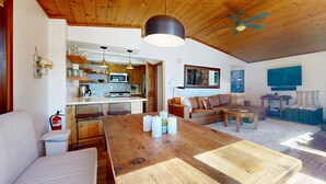 Un'ampia zona giorno con tavolo da pranzo in legno, divano, tavolino e cucina sullo sfondo.