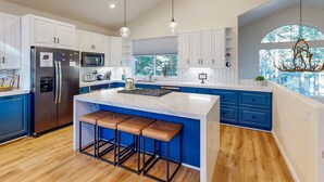Una cocina moderna con una isla grande, taburetes de bar, un refrigerador, microondas y una lámpara de araña.