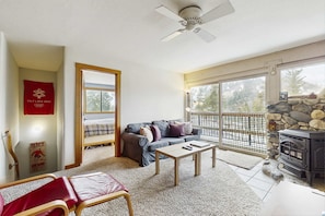 Ein Wohnzimmer mit einer Couch, einem Tisch, einem Kamin, einem Deckenventilator und Blick ins Freie.