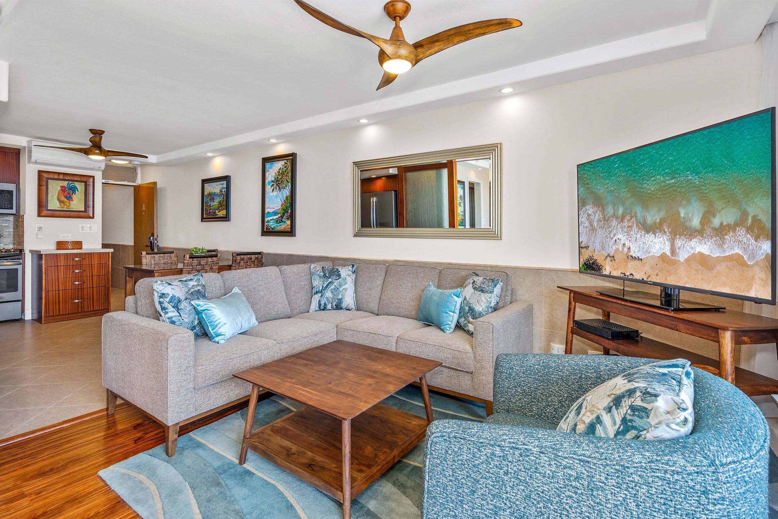 A living room with a sectional sofa, a coffee table, a TV, and a painting of a beach scene.