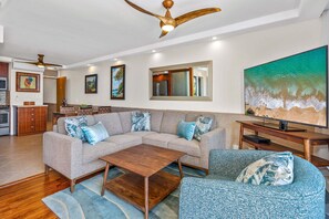 Un soggiorno con un divano componibile, un tavolino da caffè, una TV e un quadro raffigurante una spiaggia.