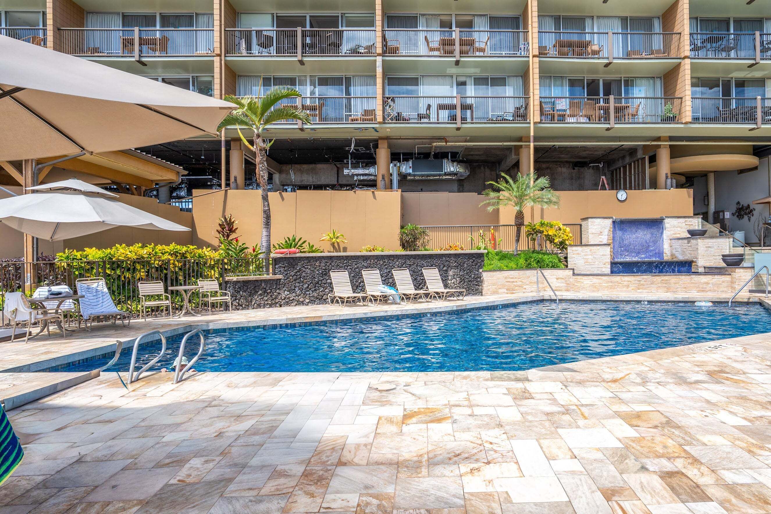A swimming pool with lounge chairs, umbrellas, and a stone wall.