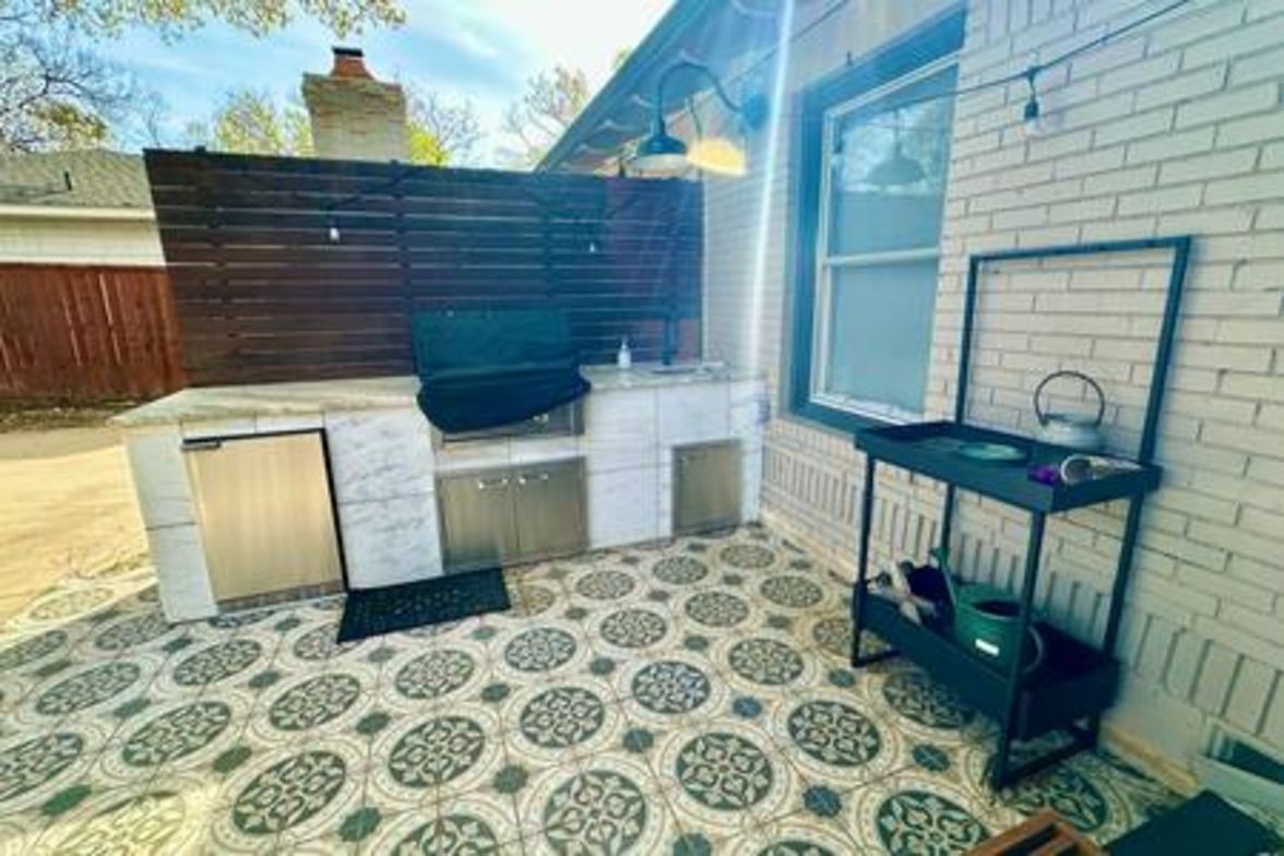 An outdoor kitchen area with a grill, a sink, and a tiled floor.