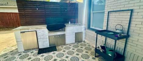An outdoor kitchen area with a grill, a sink, and a tiled floor.