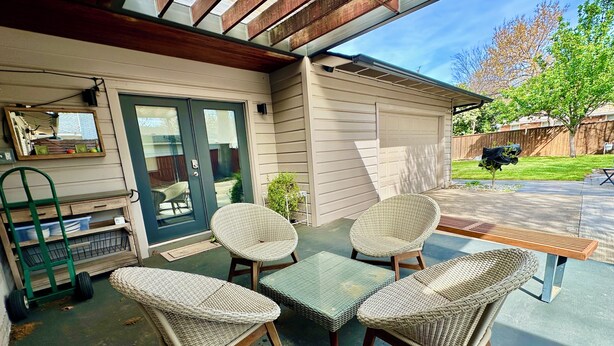 A patio with wicker furniture, a wooden table, and a green chair. - Italian Cottage Travel Nurses, Corporate Professionals - Dallas Medical District (Dallas)