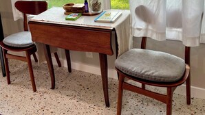 A room with a dining table, two chairs, a window with curtains, and a view of a yard. - Italian Cottage Travel Nurses, Corporate Professionals - Dallas Medical District (Dallas)