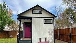A small, single-story building with a red door, a small porch with steps, and a bench outside. - Italian Cottage Travel Nurses, Corporate Professionals - Dallas Medical District (Dallas)