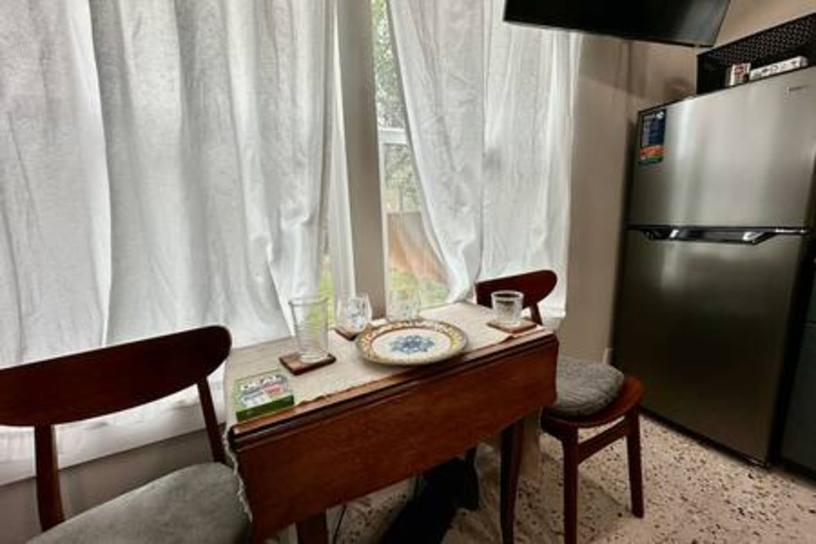 A small kitchen with a refrigerator, a table with a placemat, and two chairs.
