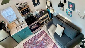 Ett kompakt bostadsutrymme med ett litet kök, en soffa, ett soffbord och en takfläkt.